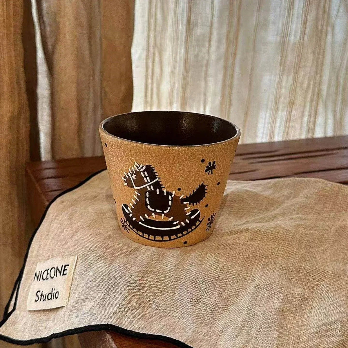 Handmade ceramic mug with playful black and white dinosaur design, resting on linen napkin
