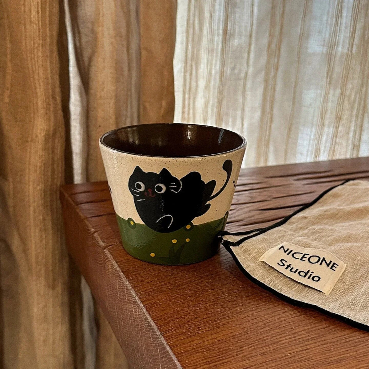 Handmade ceramic mug with black cat design, green base, on wooden shelf. Perfect for coffee or tea.